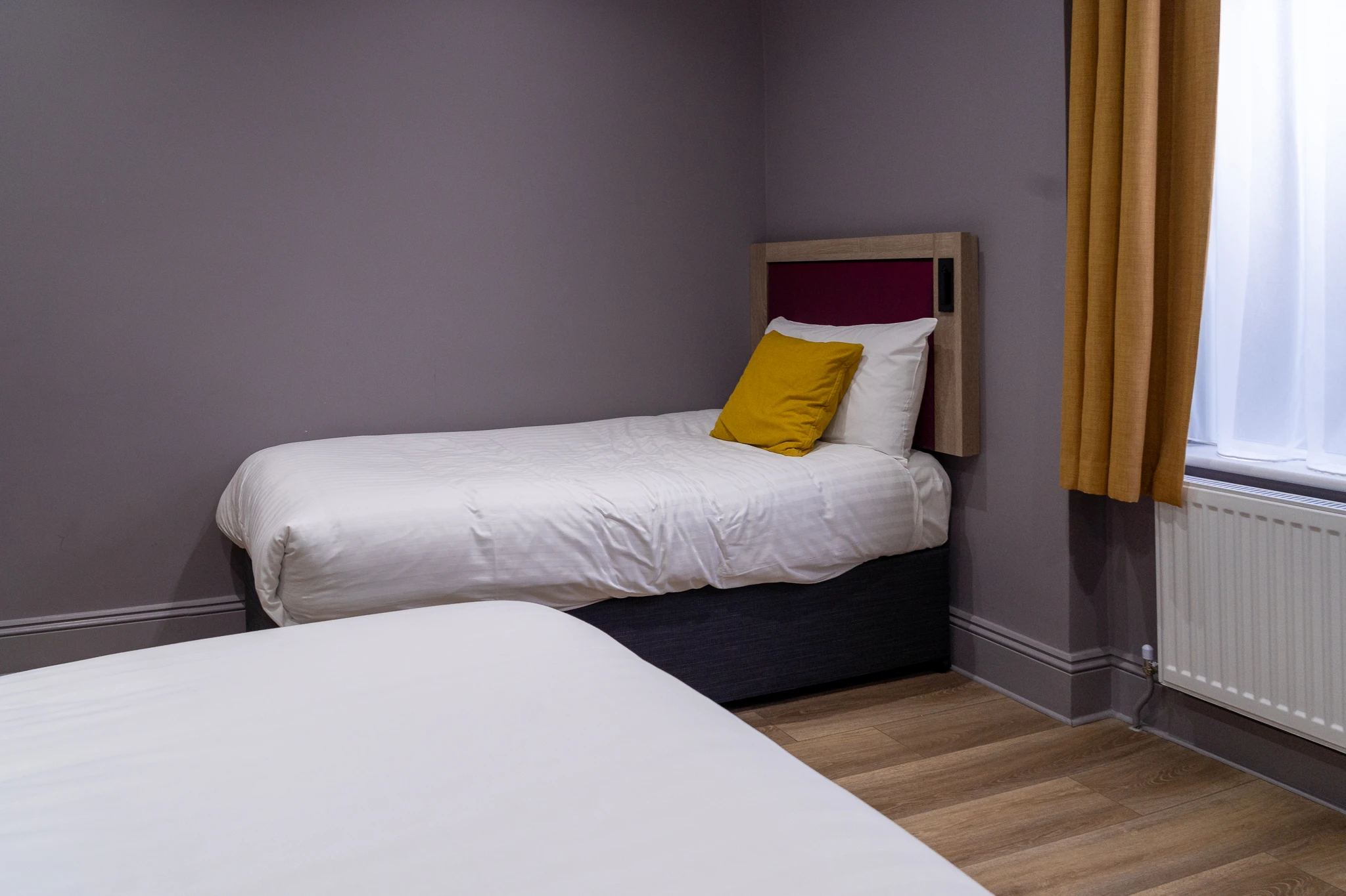 Pokój hotelowy Comfort Inn Edgware Road w Londynie, z dwoma pojedynczymi łóżkami, białą pościelą, żółtą poduszką i oknem z zasłonami.